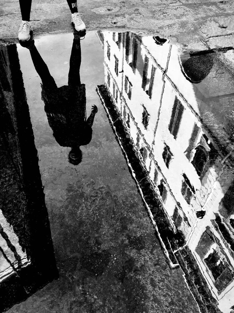 Silhouette of a woman reflected in a puddle with old buildings mirrored on the wet street in Bologna, Italy